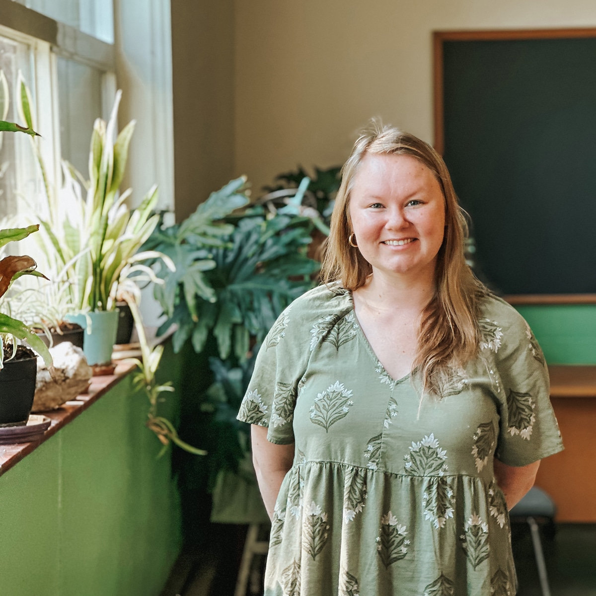 Meeri Baldwin, our Next Steps Counselor, stands next to plants in the window of a high school classroom